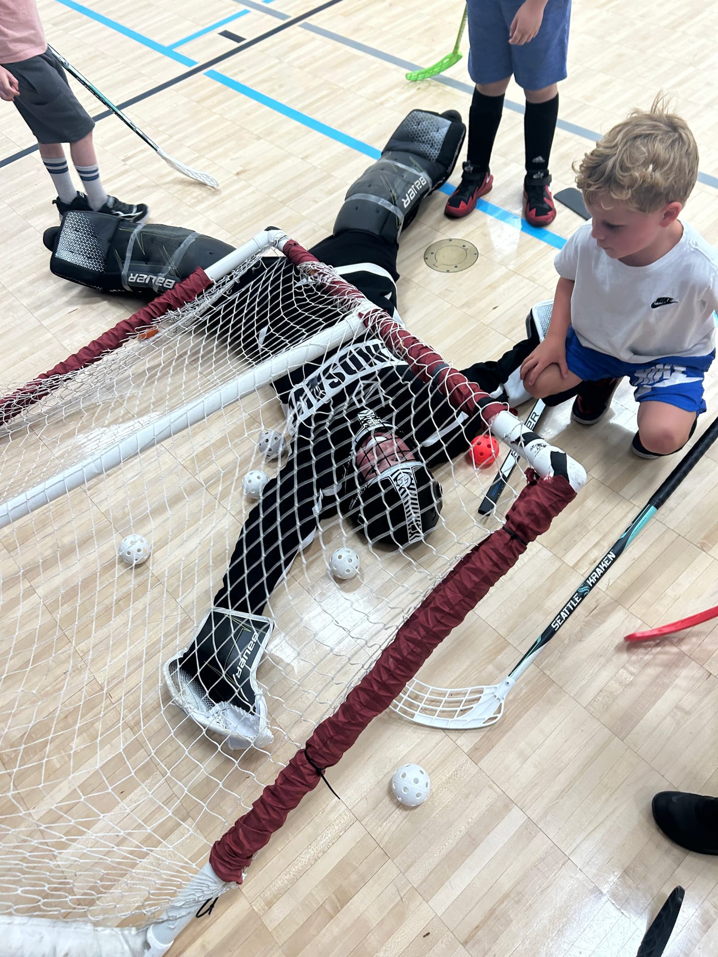 A young ECBH goalie lies on his back under the net, all smiles during Edmonds Summer Camp